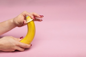 Banan og kondom på rosa bakgrunn.